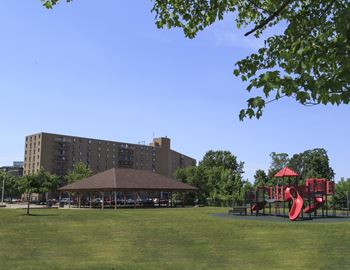 A playground with a red slide is in front of a large building.